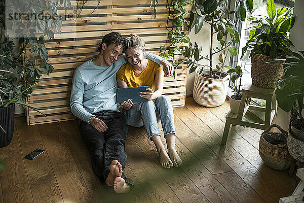 Smiling man with arm around girlfriend using tablet PC and sitting at home