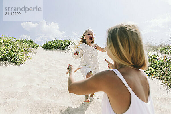 Cheerful daughter running towards mother at beach