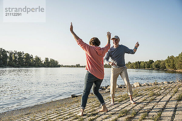 Happy senior couple dancing at riverbank on sunny day