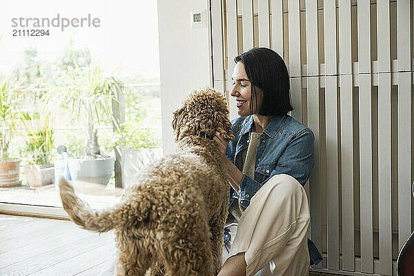 Smiling woman playing with dog at home