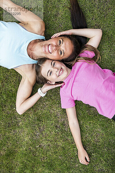 Smiling mother and daughter touching cheeks and lying down on grass in back yard