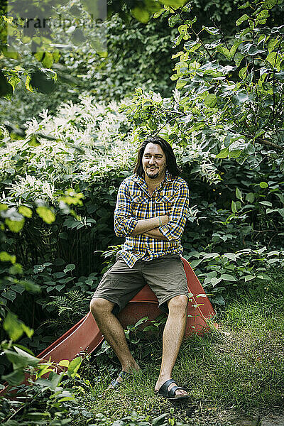 Smiling farmer with arms crossed sitting at forest