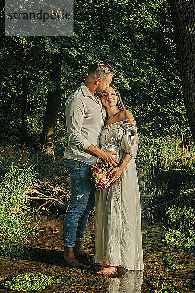 Affectionate young man with pregnant wife standing on stream