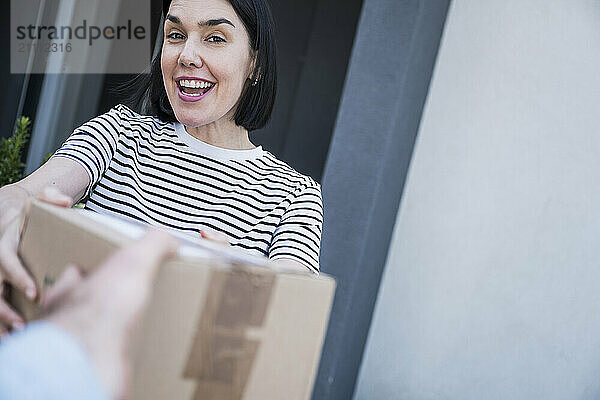 Happy woman receiving parcel from delivery person outside house