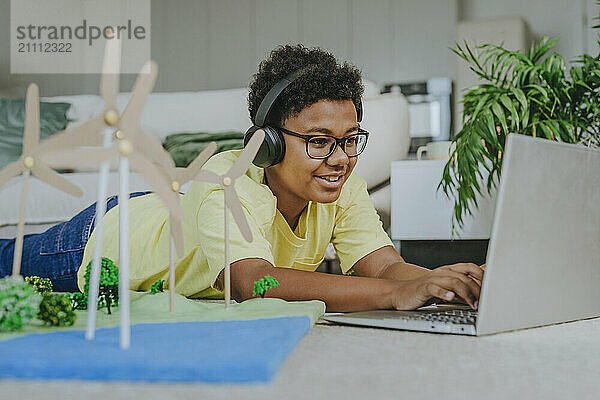 Happy boy wearing wireless headphones and using laptop near solar energy school project in living room at home