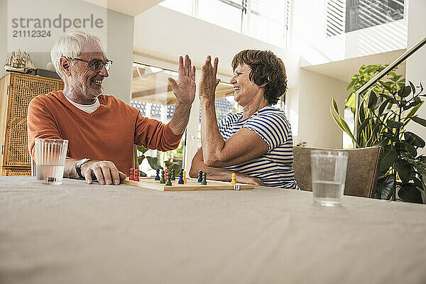 Happy senior couple gesturing high five and playing board game at home