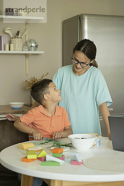 Smiling son helping mother in kitchen at home