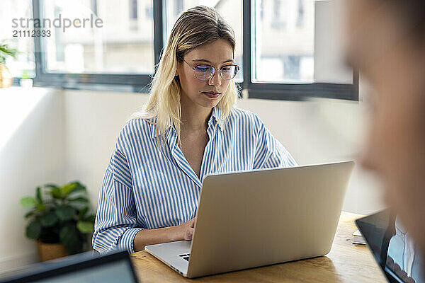 Focused blond businesswoman working on laptop in office