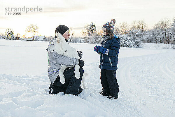 Father embracing dog near son standing in snow