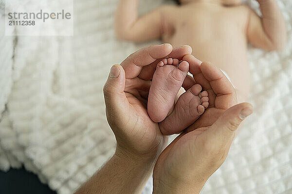 Father holding feet of new born baby lying on bed