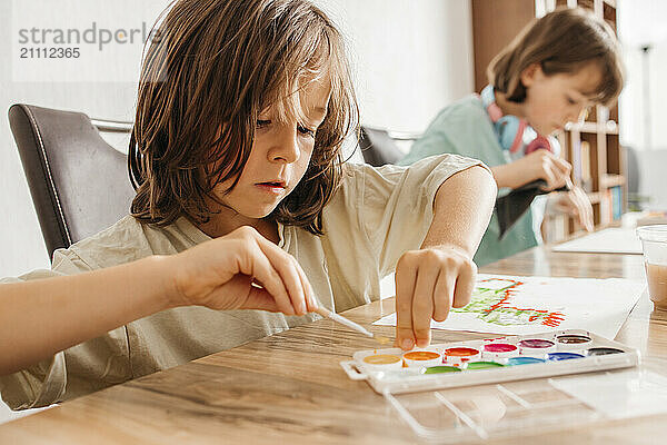 Boy using watercolor and painting with sister at home