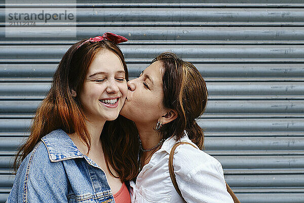 Affectionate woman kissing girlfriend in front of shutter