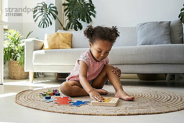 Cute girl sitting on rug and solving puzzles at home