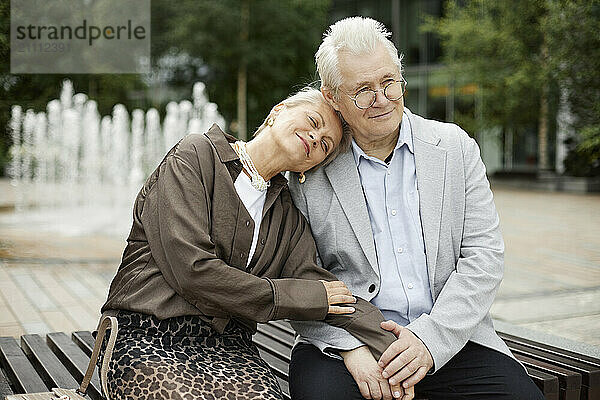 Affectionate senior couple sitting on bench at street