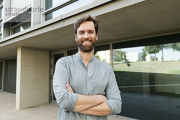 Happy business person with arms crossed standing outside office building