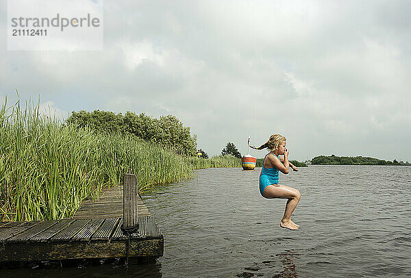 Carefree girl jumping from jetty in lake