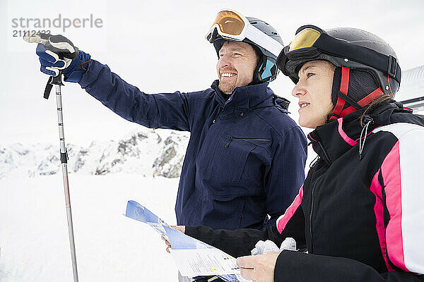 Happy man gesturing with woman holding map in winter