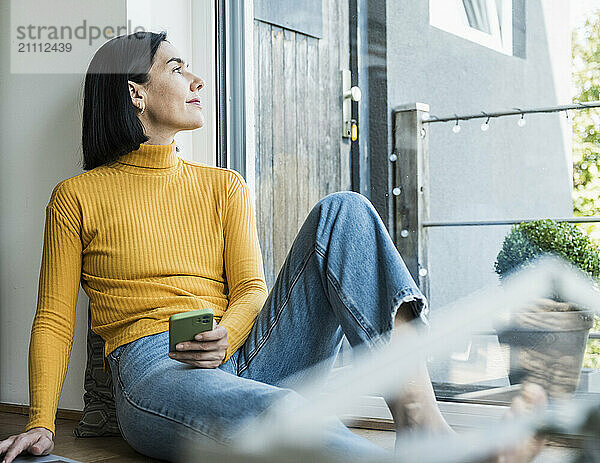 Thoughtful woman sitting with smart phone at home