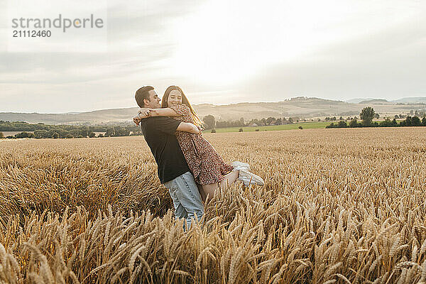 Young man picking up and embracing girlfriend in spikelet field