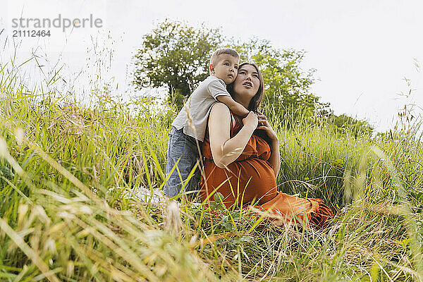 Son hugging pregnant mother in grass area