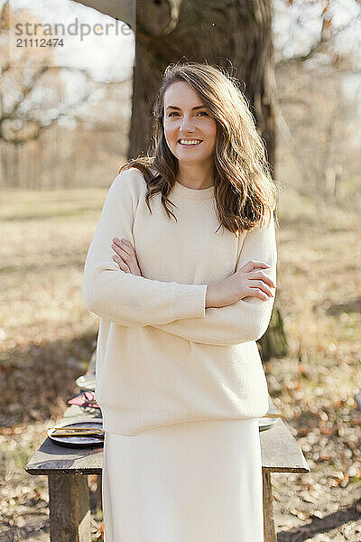 Smiling woman with arms crossed standing near table at forest