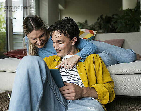 Happy young woman leaning on boyfriend using tablet PC at home