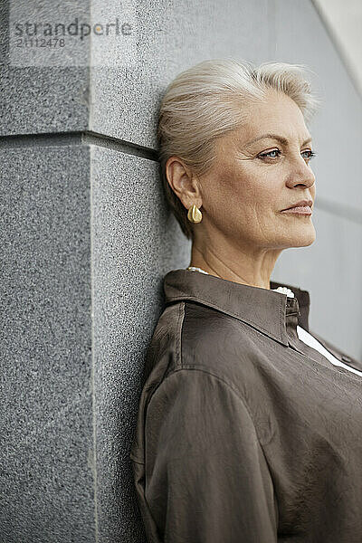 Thoughtful woman leaning on gray wall