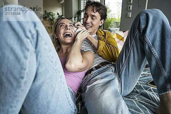 Happy young couple having fun listening to music through wireless headphones at home