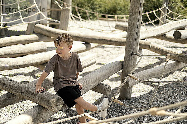 Boy sitting on wooden log in playground