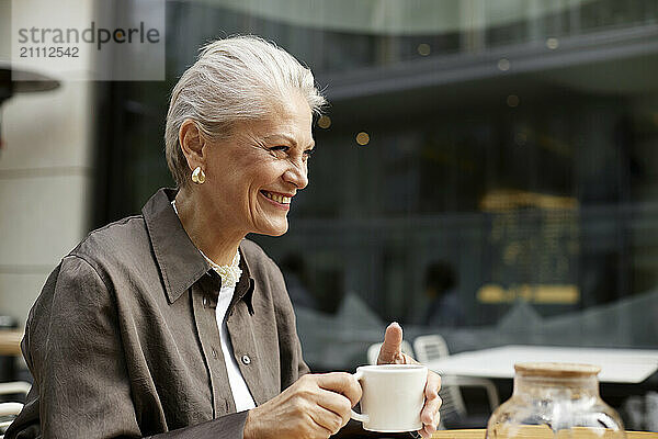 Happy woman holding tea cup and sitting at outdoor cafe