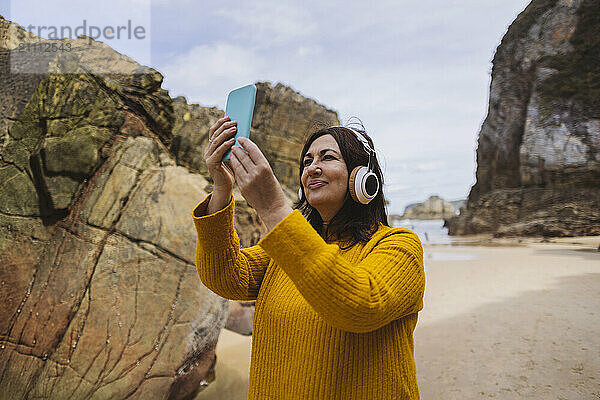 Senior woman wearing wireless headphones and listening to music on beach