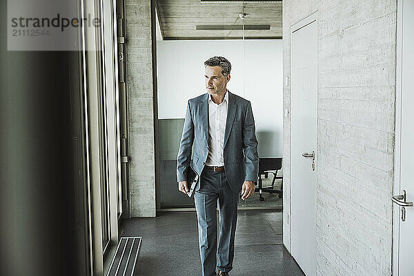 Mature businessman walking with tablet PC in office