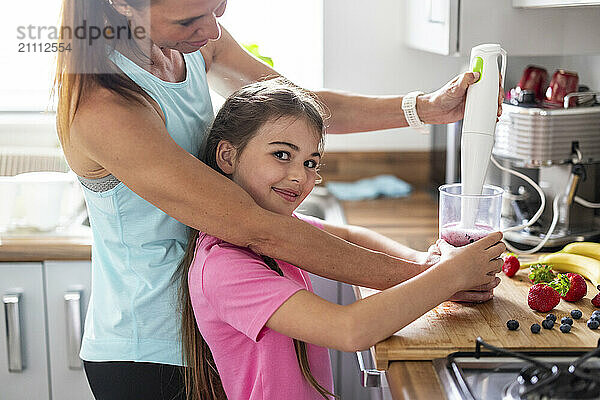 Smiling girl preparing healthy milkshake with mother at home