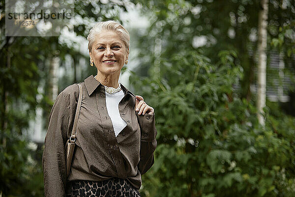 Smiling woman standing with purse in park