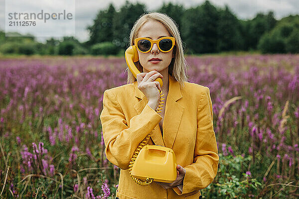 Woman in jacket talking on rotary phone near agricultural field