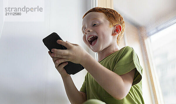 Playful boy using smart phone and enjoying at home