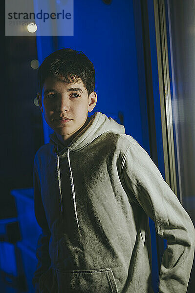 Teenage boy wearing hoodie standing near glass wall