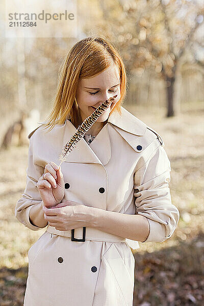 Redhead woman smelling feather and standing at forest