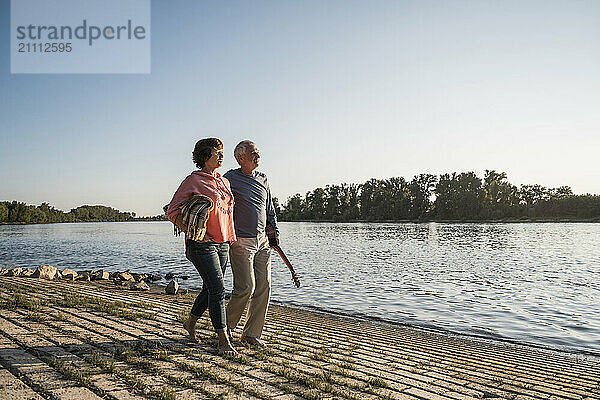 Senior couple walking at river bank on sunny day