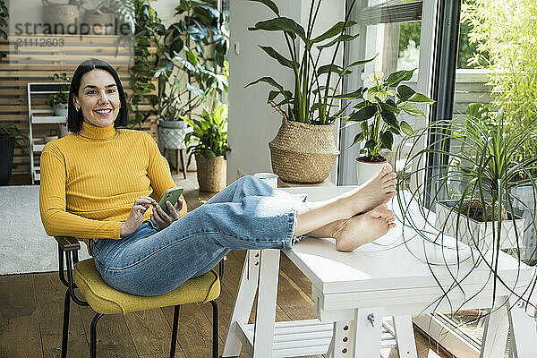 Smiling woman with feet up sitting on chair at home