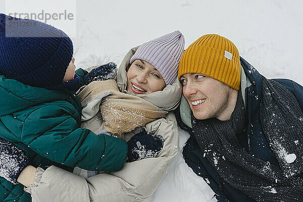 Happy parents lying down on snow with son in winter