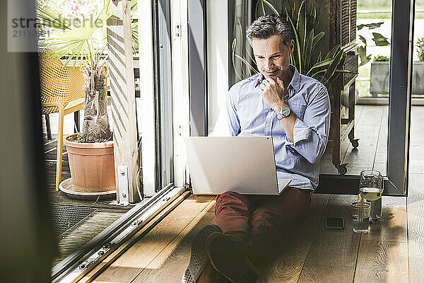 Portrait of man using laptop by open balcony