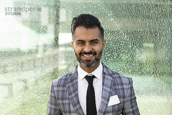 Smiling businessman in front of glass wall