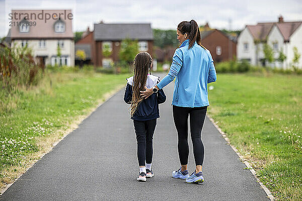 Mother and daughter in sportswear walking on footpath