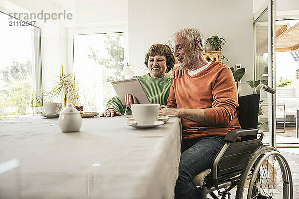 Senior man with disability sitting with wife and using digital PC at home