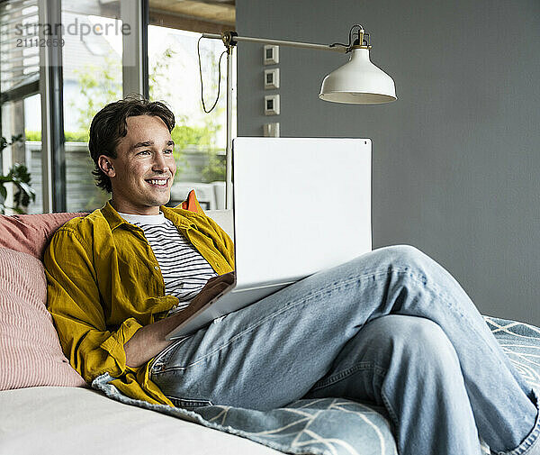 Smiling man using laptop reclining on sofa at home