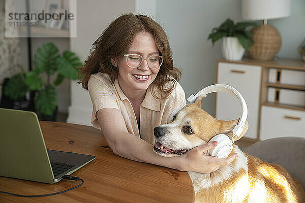 Happy woman wearing wireless headphones to dog at home