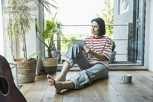 Woman using tablet PC sitting on hardwood floor at home