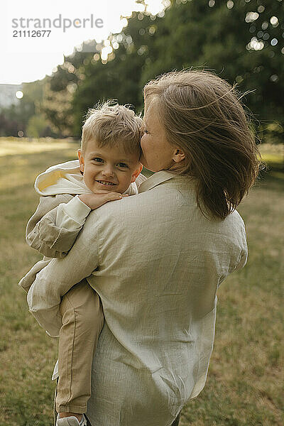 Happy mother carrying son in arms and standing at park