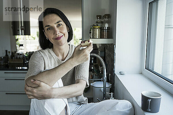 Smiling woman holding slice of cake sitting in kitchen a home